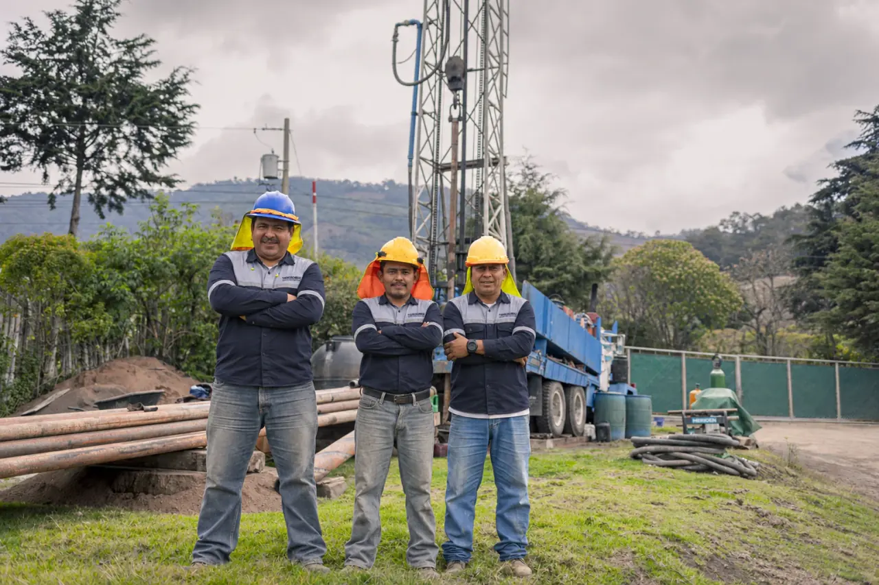 Tres perforistas con cascos junto a la perforadora en el proyecto Pozo Calderas